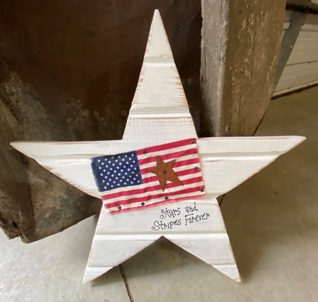 Wooden white star with flag, rusty star, and words "stars and stripes forever"