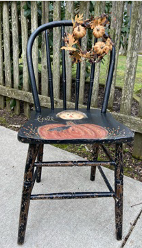 Black wooden chair with painted pumpkin and scarecrow head on the seat