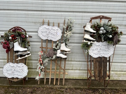 picture of small sled on left with winter decorations; middle is decorative fencing with skates and skate rental sign, right is large sled with same decorative skates, greenery, and skate rental sign