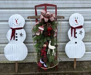 two white metal snowmen on sticks and an antique wooden sled with greens, bells, ribbing and mittens on it