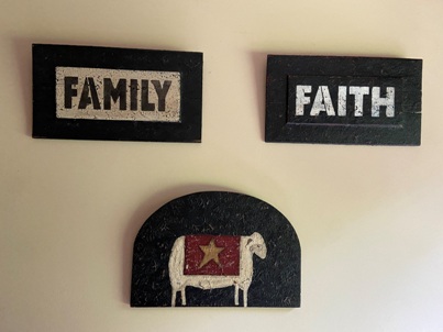 Three wooden signs hand painted. One with the word family, one with the word faith and one with a sheep on it.