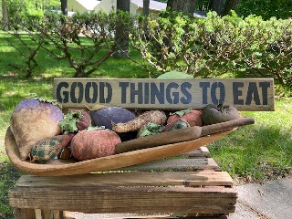 Wooden stenciled sign that says "Good Things to Eat" sitting in a primative bowl of fabric fruit