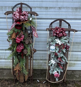Two antique wooden sleds decorated with bows, greenery, mittens, bells and seasonal items